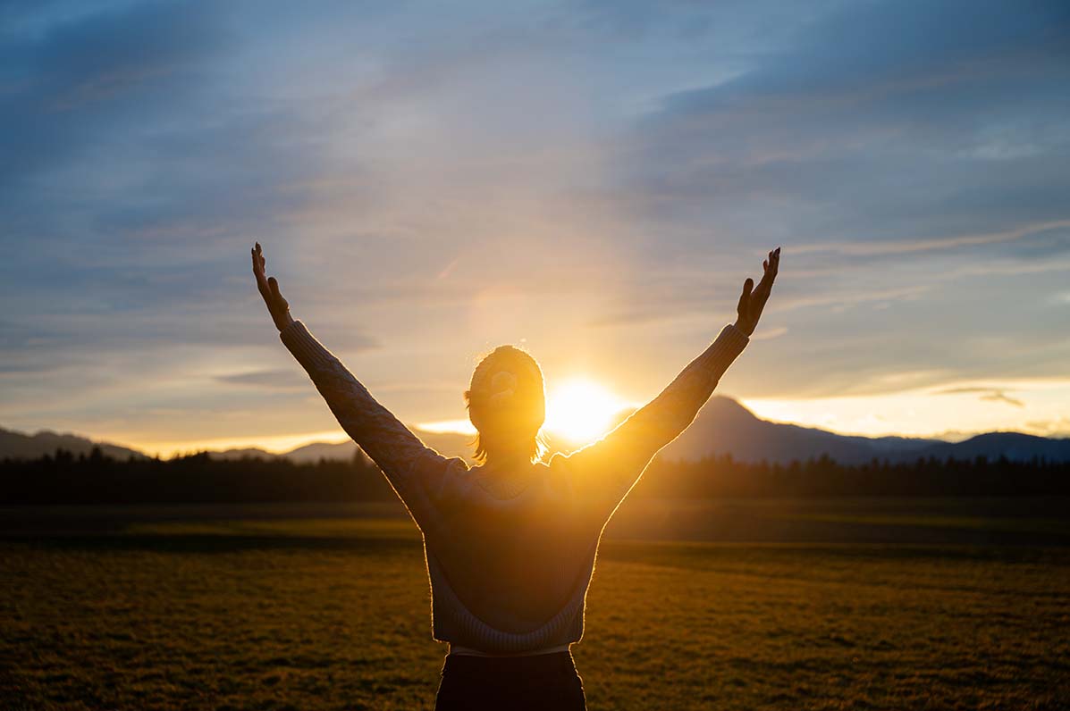 woman with hands up in field at sunset, embracing life