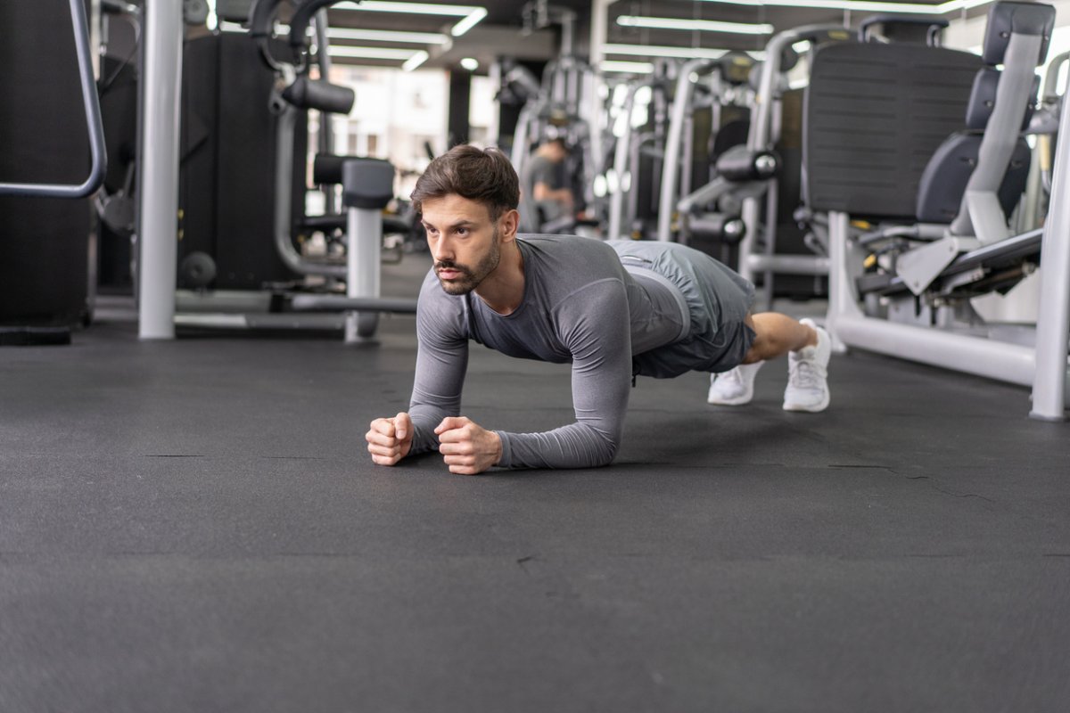 Man in gray workout clothes doing a plank in a gym.